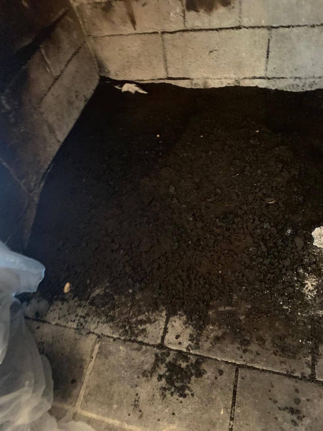 A firebox floor covered in soot and debris, between light firebrick walls.