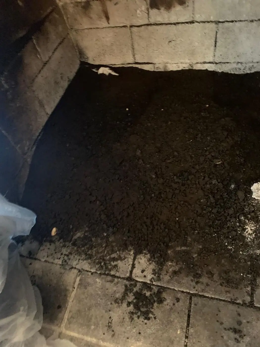A firebox floor covered in soot and debris, between light firebrick walls.