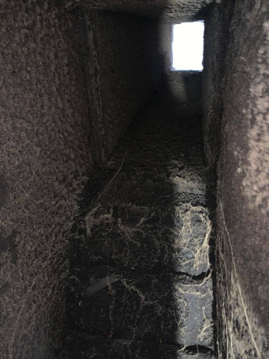 Looking up a soot-coated flue toward the daylight at the top, with cobwebs on the walls.